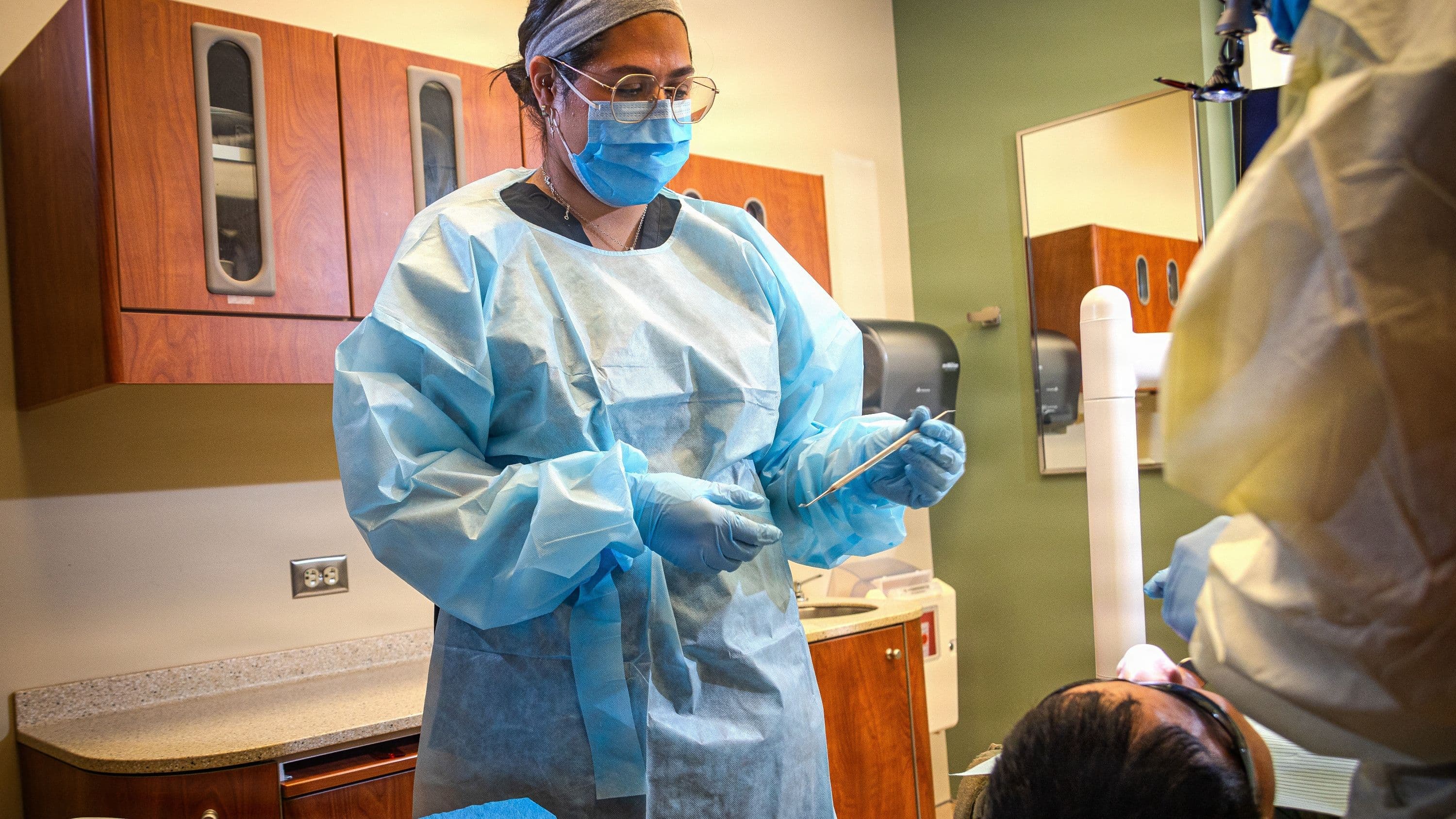 Dental assistant holds a dental tool standing over a patient.
